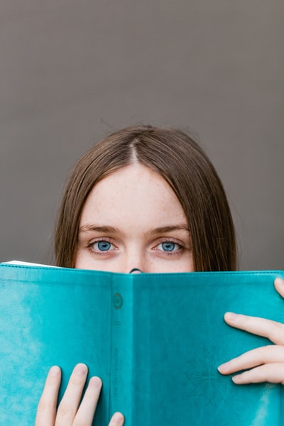 Cover your face with a bluish green book of woman
